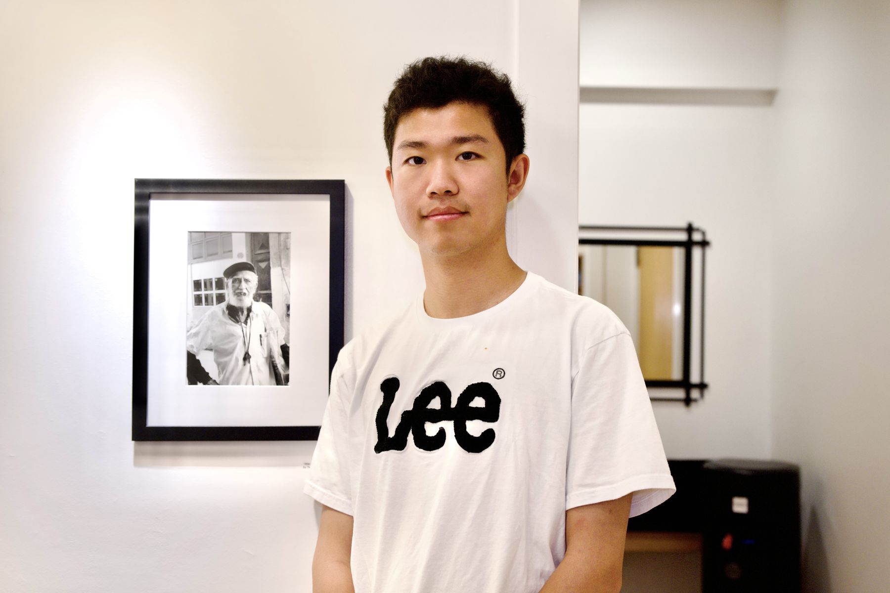Thomas standing beside his framed black-and-white portrait print on a white wall