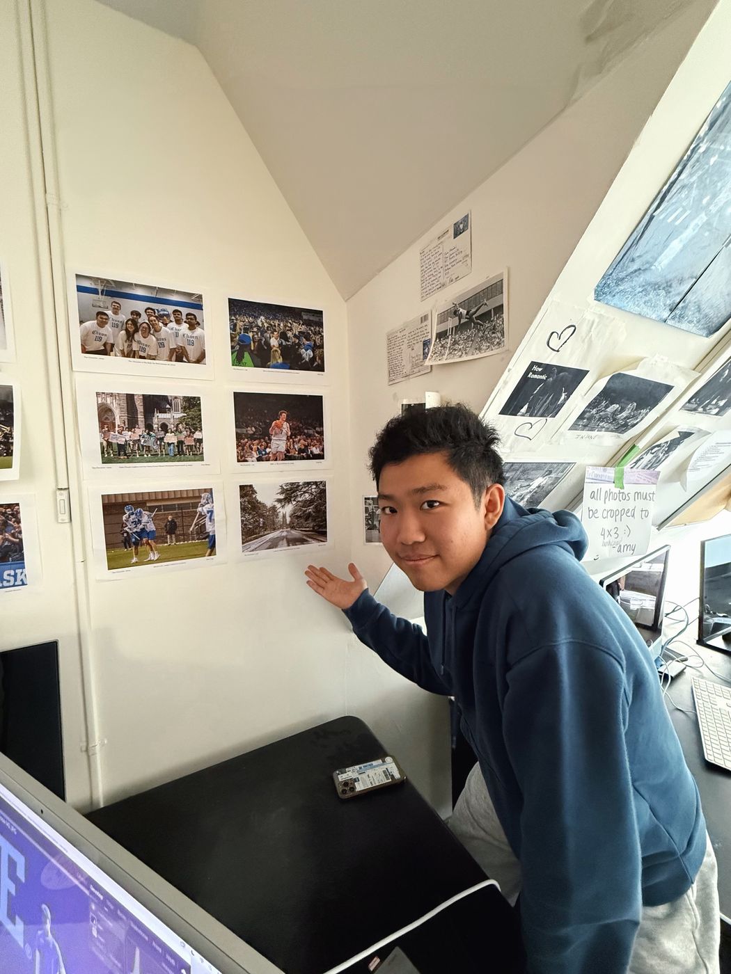 Thomas pointing to one of several printed photographs pinned to a wall