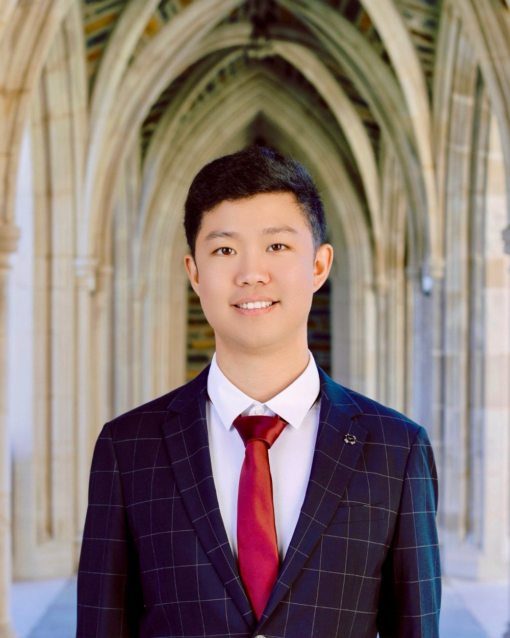 Thomas Han in a suit and red tie, standing in a stone cloister with pointed arches
